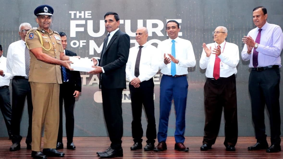 Officials and police officers on stage during a formal award ceremony, presenting digital card as others applaud